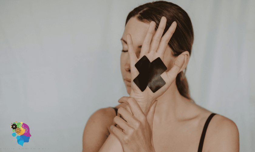 Woman with a black cross on her palm covering face, symbolizing silence in trauma responses in relationships.